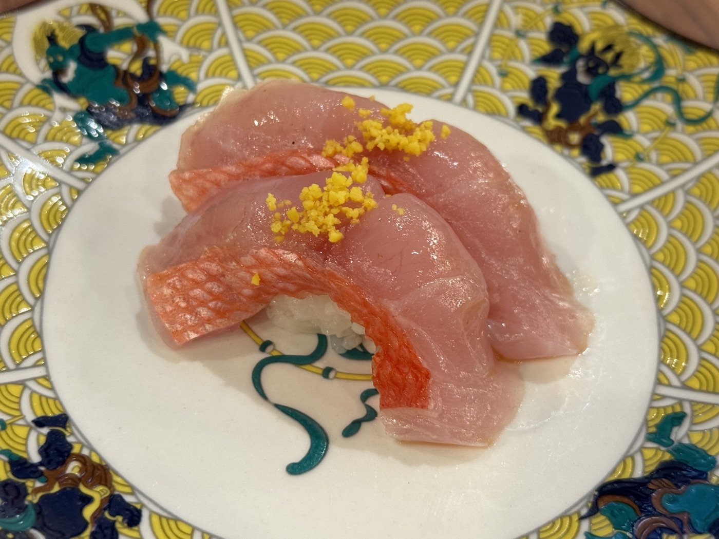 Two pieces of pink fish nigiri with yellow garnish on a patterned ceramic plate