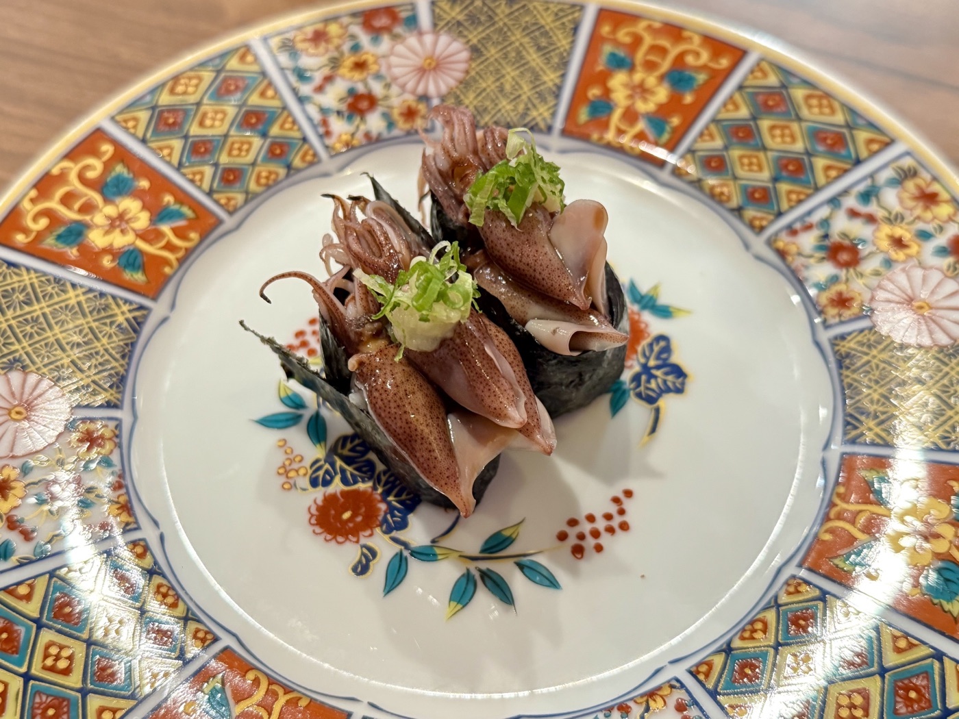 Two squid sushi pieces topped with chopped green onion on a colorful patterned plate
