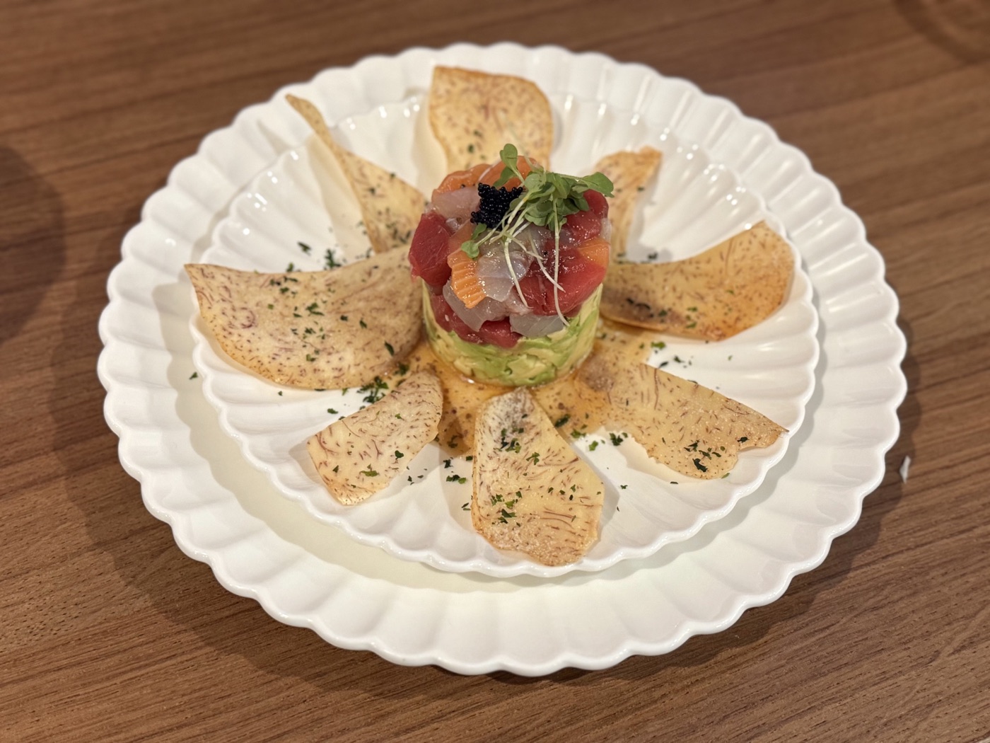 Diced fish and avocado stacked at the center of a white plate surrounded by crisp chips
